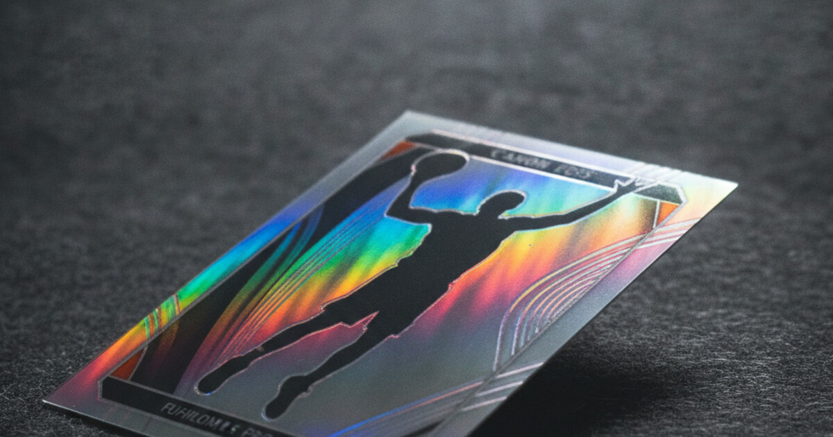 A Topps Chrome sports card tilted at an angle under bright light showing a vivid rainbow prismatic refractor shimmer across the card surface